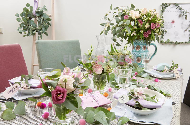 Trend Eukalyptus - gedeckter Tisch mit Blüten (Alstromerien, Rosen, Lisianthus) und Eukalyptusblättern, künstlicher Kranz an Dekoleiter und Bild mit Eukalyptusrahmen